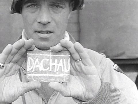 Ein Mann hält ein kleines Schild mit der Aufschrift "Dachau" hoch. (Foto: SWR - Screenshot aus der Sendung)
