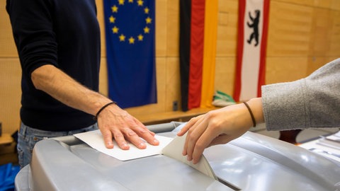 Jemand wirft seinen Stimmzellel in die Wahlurne im Wahllokal: Bei der Bundestagswahl 2025 geht es um die Bildung einer neuen Regierung
