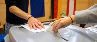 Jemand wirft seinen Stimmzellel in die Wahlurne im Wahllokal: Bei der Bundestagswahl 2025 geht es um die Bildung einer neuen Regierung