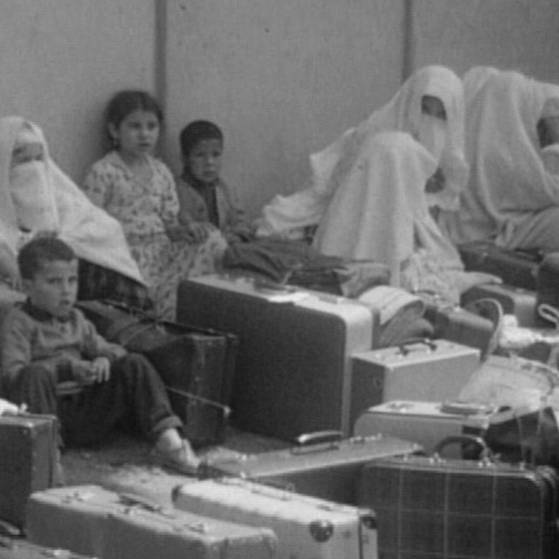 Schwarz-weiß Bild von Frauen und Kindern, die auf der Straße sitzen mit vielen Koffern im Vordergrund.