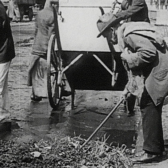 Mann stochert mit Stock in Abfallhaufen