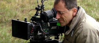 Ein Mann steht hinter einer Kamera im grünen.