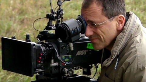 Ein Mann steht hinter einer Kamera im grünen.