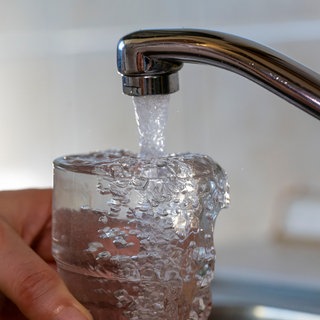 Wasser läuft aus einem Wasserhahn in ein Glas
