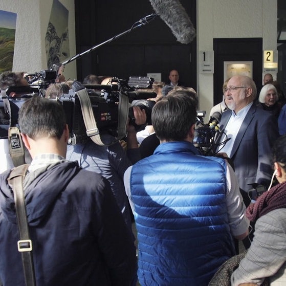 Jürgen Grässlin umringt von Reportern. (Foto: SWR – Screenshot aus der Sendung)