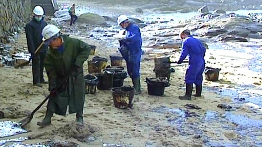 Männer reinigen einen Strand, auf dem Erdöl klebt.