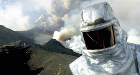 Im Vordergrund ein Forscher mit Brandschutzanzug, im Hintergrund rauchende Schlote eines Vulkans. (Foto: dpa)