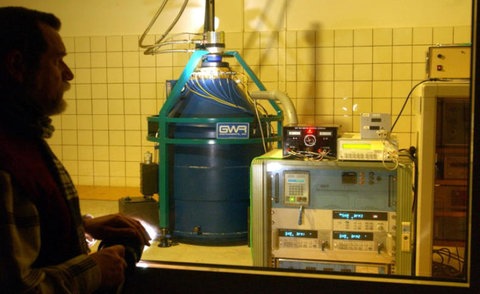 Im Vordergrund ein Forscher mit Brandschutzanzug, im Hintergrund rauchende Schlote eines Vulkans.