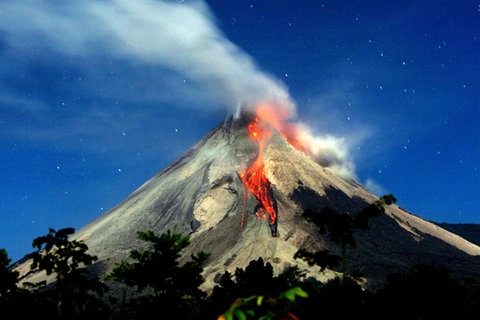 Blick auf den Vulkankegel des Merapi. Der Schlot raucht, an seiner Flanke fließt glühende Lava herab.