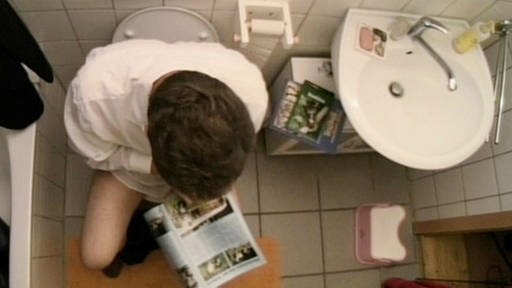 Blick von oben auf einen Mann, der auf der Toilette sitzt und eine Zeitschrift liest. (Foto: SWR/WDR)