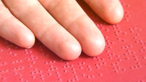Finger auf rotem Blatt mit Brailleschrift.