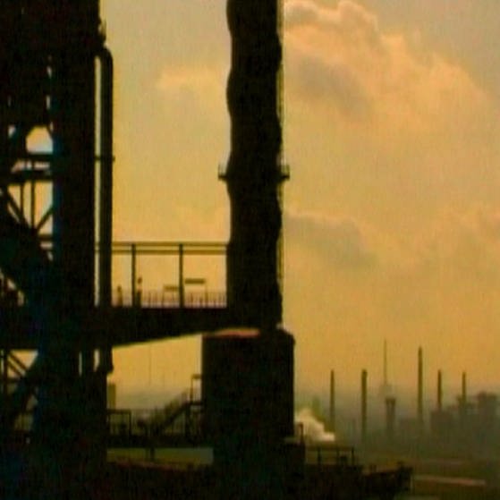 Eine Stahlkonstruktion im Vordergrund und einem Industriekomplex im Hintergrund mit hohen Schornsteinen. (Foto: SWR – Screenshot aus der Sendung)