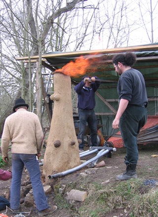 Ein Mann pumpt mit einem großen Blasebalg Luft in einen Rennofen.