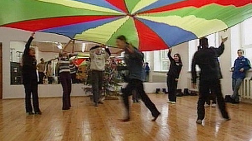 Mehrere Personen stehen in einem Kreis und halten ein buntes Tuch hoch.