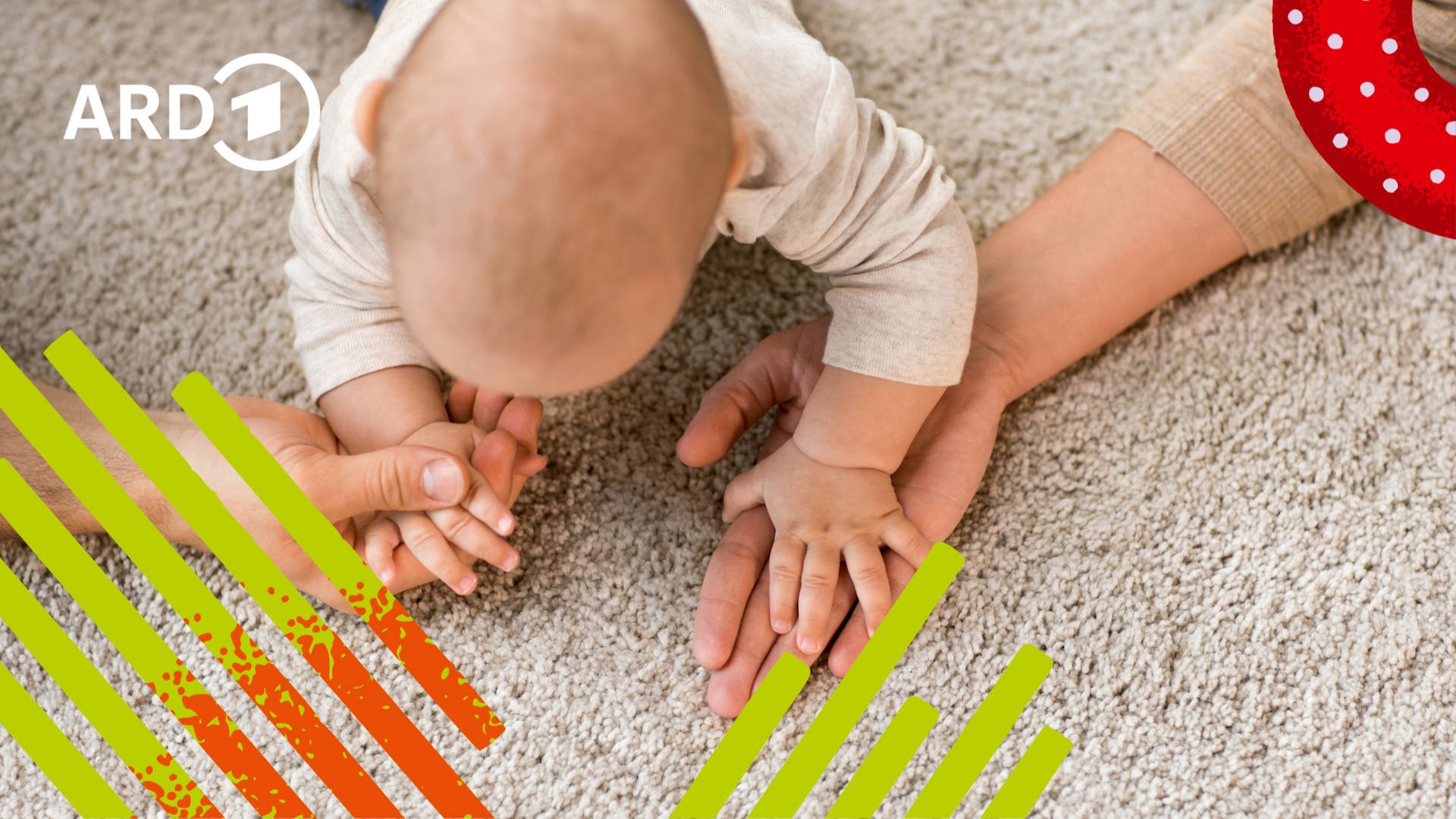 Ein Baby auf dem Boden greift nach den Händen seiner Eltern.
