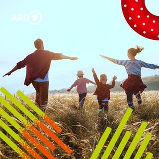 Eltern mit zwei Kindern laufen bei Sonnenuntergang auf einer Wiese.