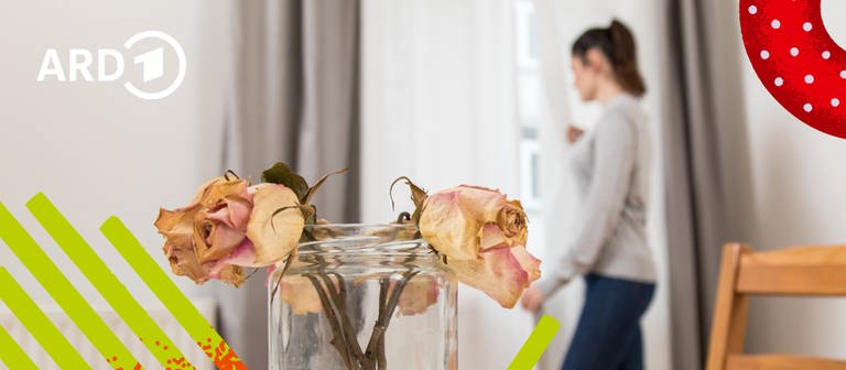Zwei verwelkte Rosen in einer Vase auf einem Esstisch und eine Frau im Hintergrund, die traurig aus dem Fenster sieht. (Foto: picture alliance / dpa Themendienst | Christin Klose/Bildmontage:BR)