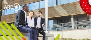 Eine Gruppe Menschen sitzt im Innenhof eines Bürogebäudes und unterhält sich.