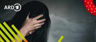 Ein Mensch sitzt am Tisch im Dunklen und verkrampft die Hände vor Angst