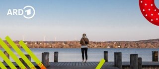 Eine Frau steht allein auf einem Steg am See und sieht in die Ferne.