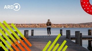 Eine Frau steht allein auf einem Steg am See und sieht in die Ferne.