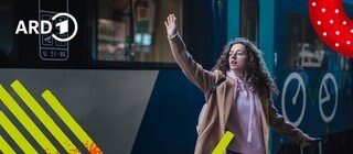 Eine junge Frau steht mit einem Koffer am Bahnhof vor einem Zug und winkt zum Abschied in die Ferne.