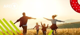 Eltern mit zwei Kindern laufen bei Sonnenuntergang auf einer Wiese.