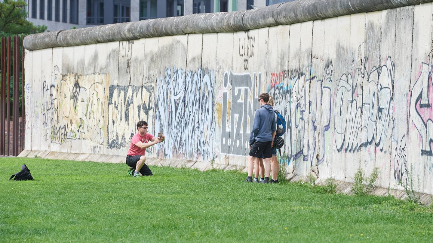 Menschen machen Fotos an Resten der Berliner Mauer. Die Teilung Deutschlands hat das Leben vieler in Ost und West geprägt. (Foto: IMAGO / epd)