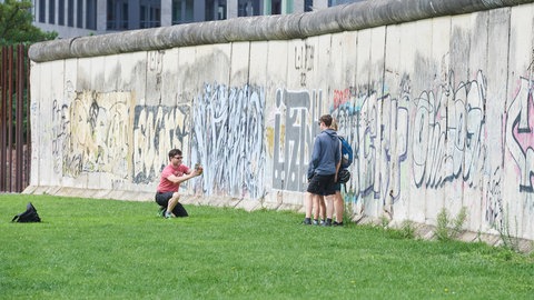 Menschen machen Fotos an Resten der Berliner Mauer. Die Teilung Deutschlands hat das Leben vieler in Ost und West geprägt.