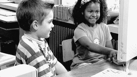 Schwarz-weiß Bild von zwei Kindern, die vor einem Computer sitzen.