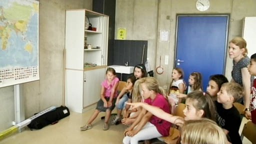 Grundschüler im Halbkreis, im Hintergrund die Lehrerin. (Foto: SWR – Screenshot aus der Sendung)