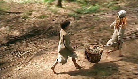 Till und Ronja tragen einen Korb mit frisch geerntetem Getreide ins Dorf.