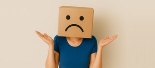 Diese Seite existiert nicht mehr! Enttäuschte Frau mit einem Pappkarton mit einem traurigen Smiley auf dem Kopf.