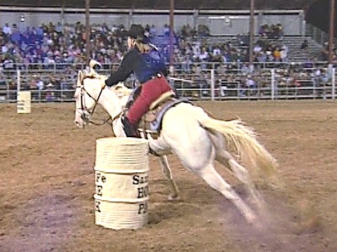 Barrel racing: Eine Frau auf einem weißem Pferd umreitet eine Tonne. [Klick auf das Bild, schließt das Fenster]