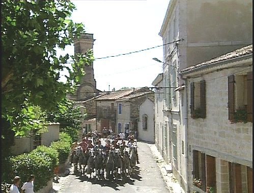 Einige Personen zu Pferd reiten über eine Dorfstrasse [Klick auf das Bild, schließt das Fenster]