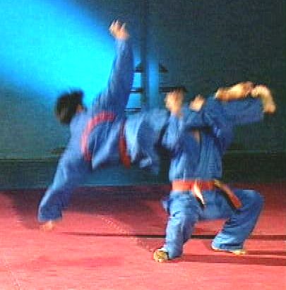 Ein Kämpfer schlingt im Sprung seine Beine um den Hals des Gegners (Beinschere) um ihn zu Boden zu reißen [Klick auf das Bild, schließt das Fenster]