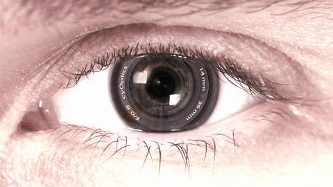 Es ist ein Auge zu sehen, bei dem die Pupille durch eine Kameralinse ersetzt ist. (Foto: SWR/MDR – Screenshot aus der Sendung)