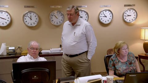 Ein Mann steht in einem Kontrollraum mit vielen Uhren und schaut einem Kollegen über die Schulter auf den Bildschirm. (Foto: SWR - Screenshot aus der Sendung)