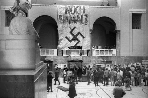 Studenten versammeln sich in Uni-Aula; an der Wand: Transparent mit Hakenkreuz und Aufschrift „Noch einmal?“ (Foto: imago images / Heinz Gebhardt)
