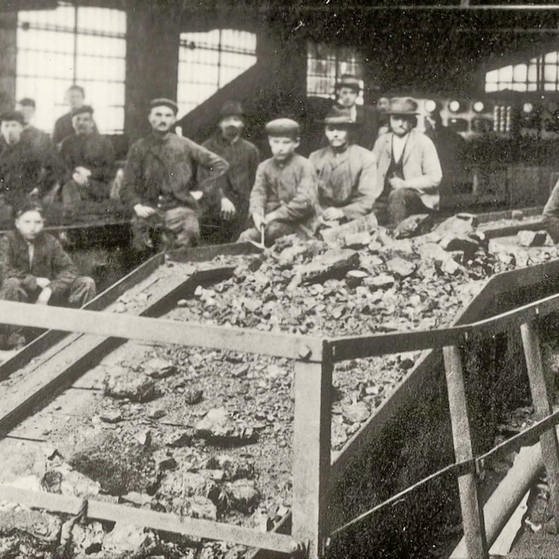 Schwarzweiß-Aufnahme : Minenarbeit in Fabrikgebäude an einem Förderband. (Foto: SWR – Screenshot aus der Sendung)