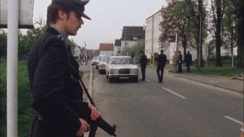 Polizist mit Maschinengewehr bewacht eine Straße (Foto: SWR - Screenshot aus der Sendung)