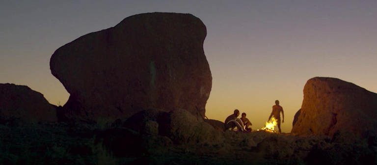 Menschen sitzen zwischen Felsen im Sonnenuntergang. (Foto: SWR – Screenshot aus der Sendung)