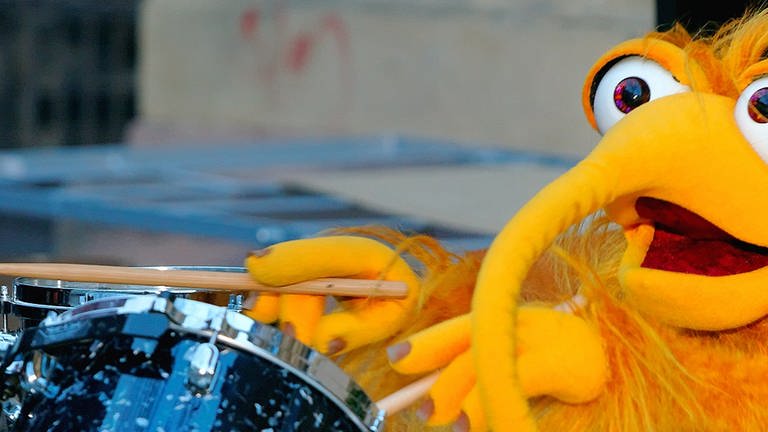 Eine gelbe Plüschpuppe spielt auf einem Schlagzeug. (Foto: SWR)