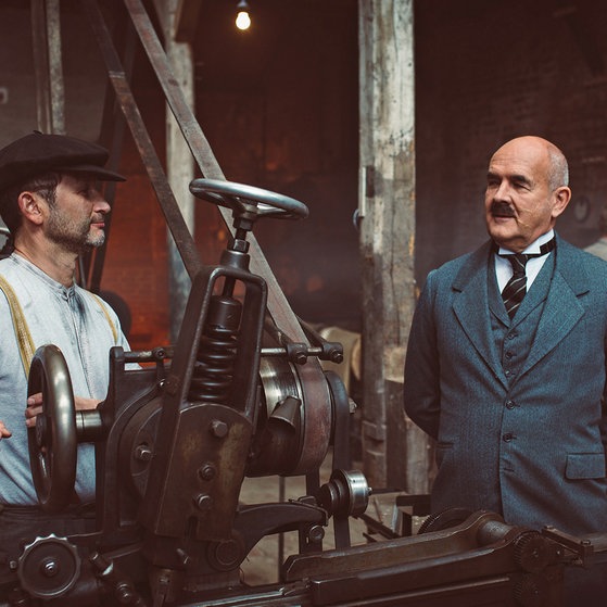 Spielszene: Röchling in Anzug in der Fabrik, neben ihm ein Arbeiter. (Foto: SWR/moving story media/Hans Jacobi)