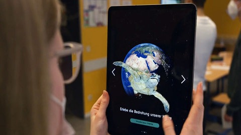 Eine Schülerin nutzt die WDR Klima-App auf einem Tablet, das eine Weltkugel und eine Schildkröte zeigt