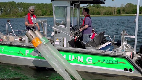 Ein kleines Forschungsboot mit zwei Wissenschaftlern an Bord. Von der Seite hängen zwei schlauchartige Planktonnetze ins Wasser.