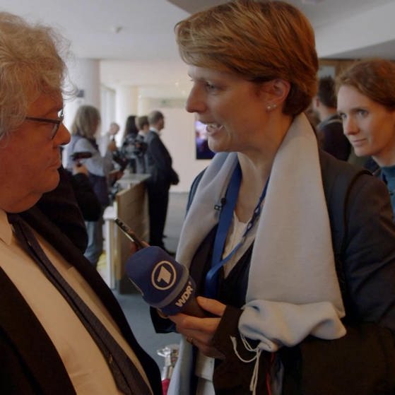 Astrid Corall mit Mikrofon interviewt einen Europa-Abgeordneten.