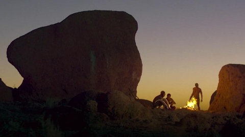 Menschen sitzen zwischen Felsen im Sonnenuntergang.