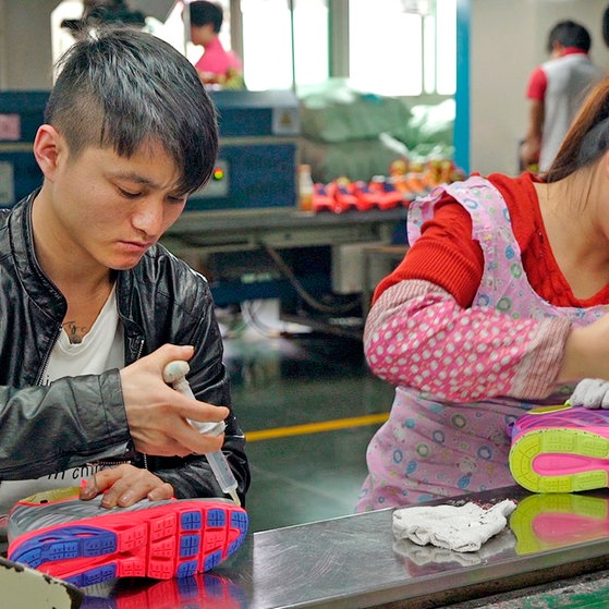 Ein Mann und eine Frau tragen mit Spritzen Klebstoff auf Turnschuhe auf.