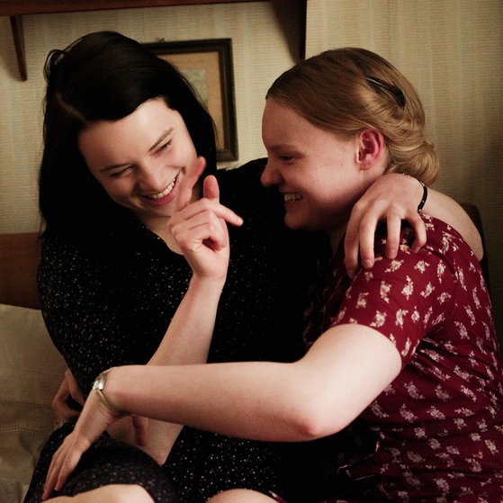 Spielszene: Sophie und Inge sitzen auf einem Bett und lachen.
